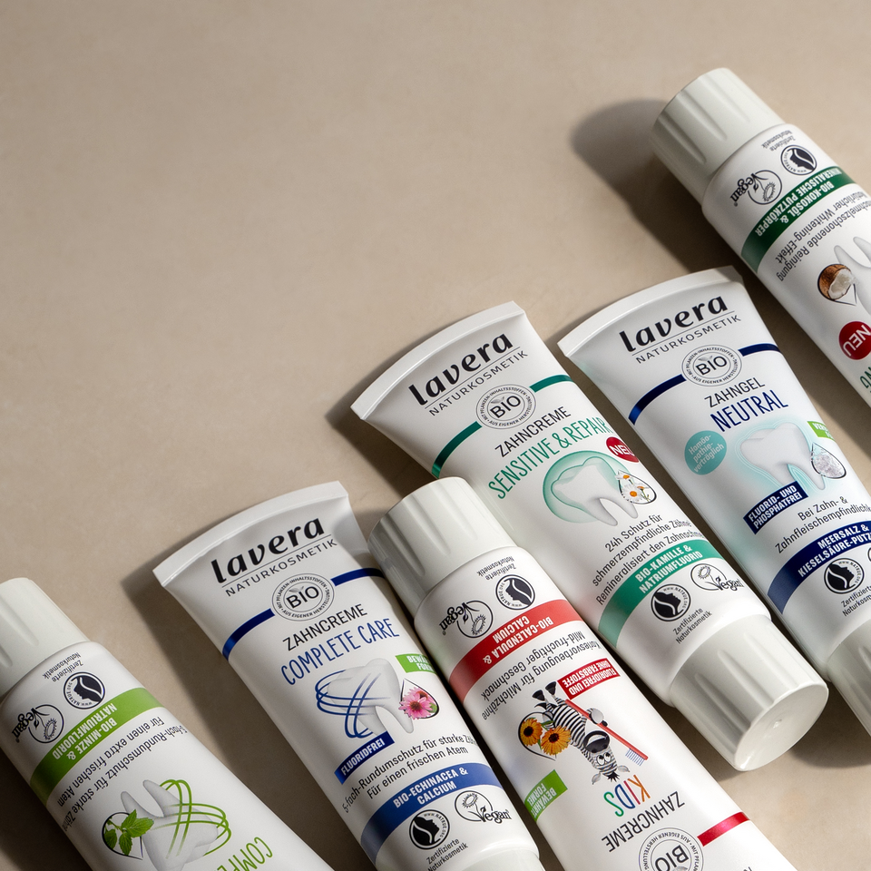 Flatlay: lavera Zahnpflegeprodukte, Zahncremes und Zahngel auf beigem Hintergrund