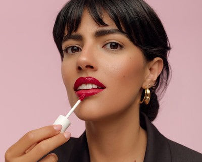 Donna applica rossetto liquido rosso davanti a sfondo rosa