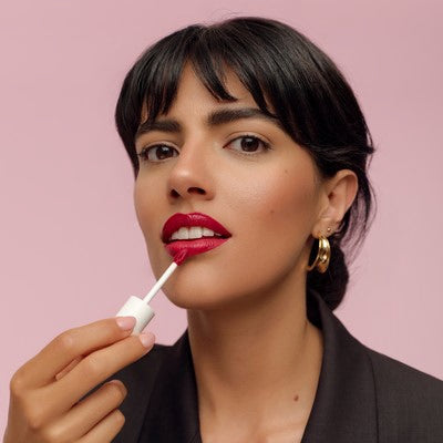 Donna applica rossetto liquido rosso davanti a sfondo rosa