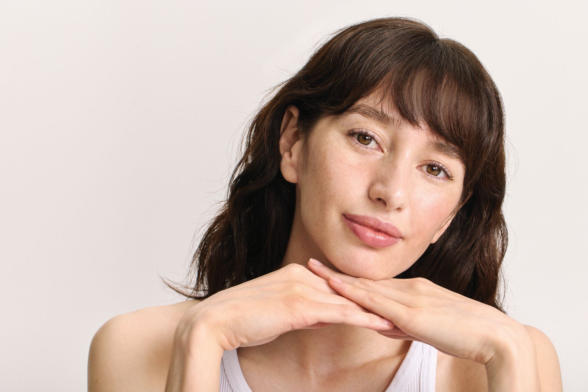 Frau mit natürlichem Look und gepflegten Lippen, die die Hände unter das Kinn legt.