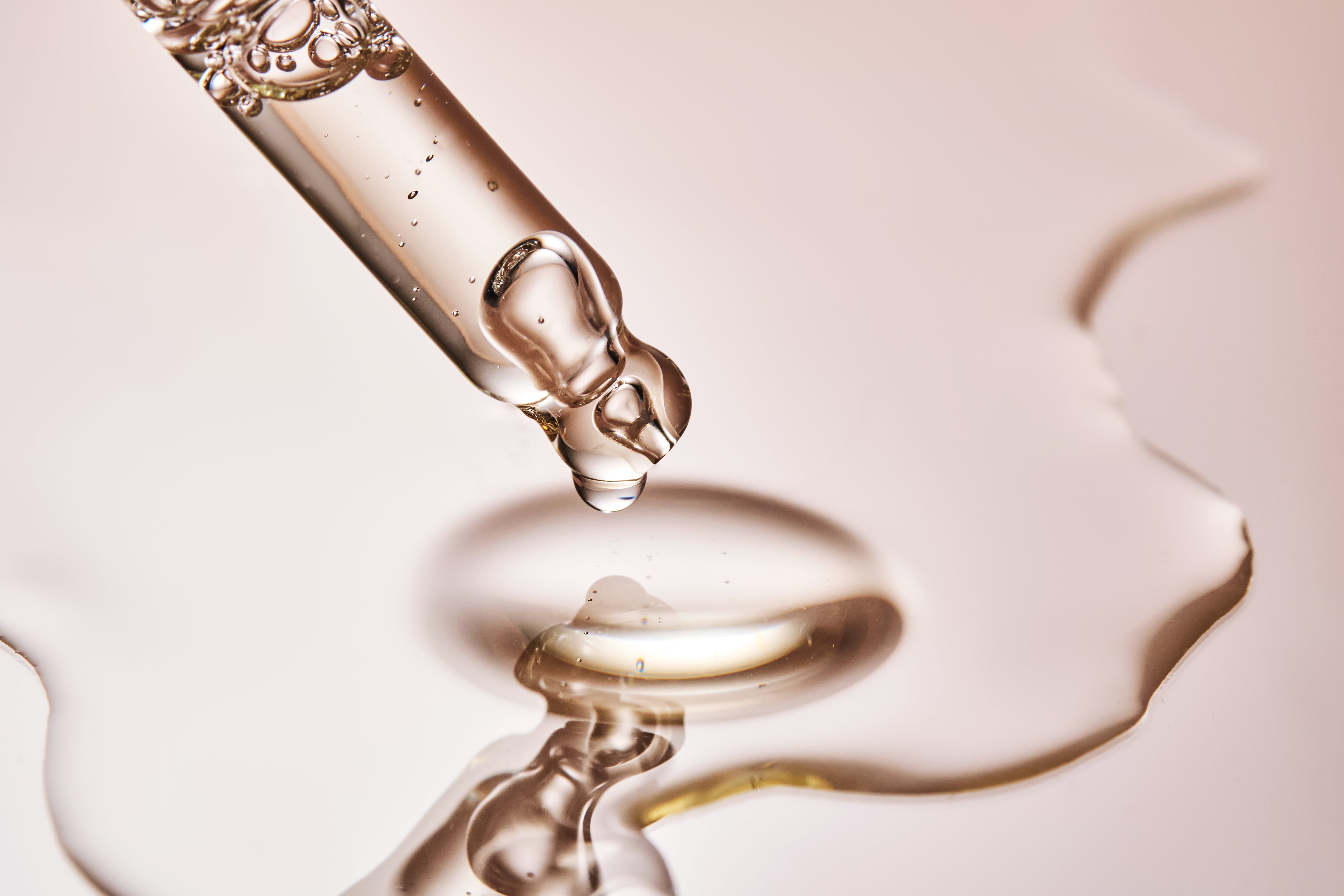 durchsichtige Flüssigkeit in einer Pipette, getropft auf einem rose-goldenen Hintergrund
