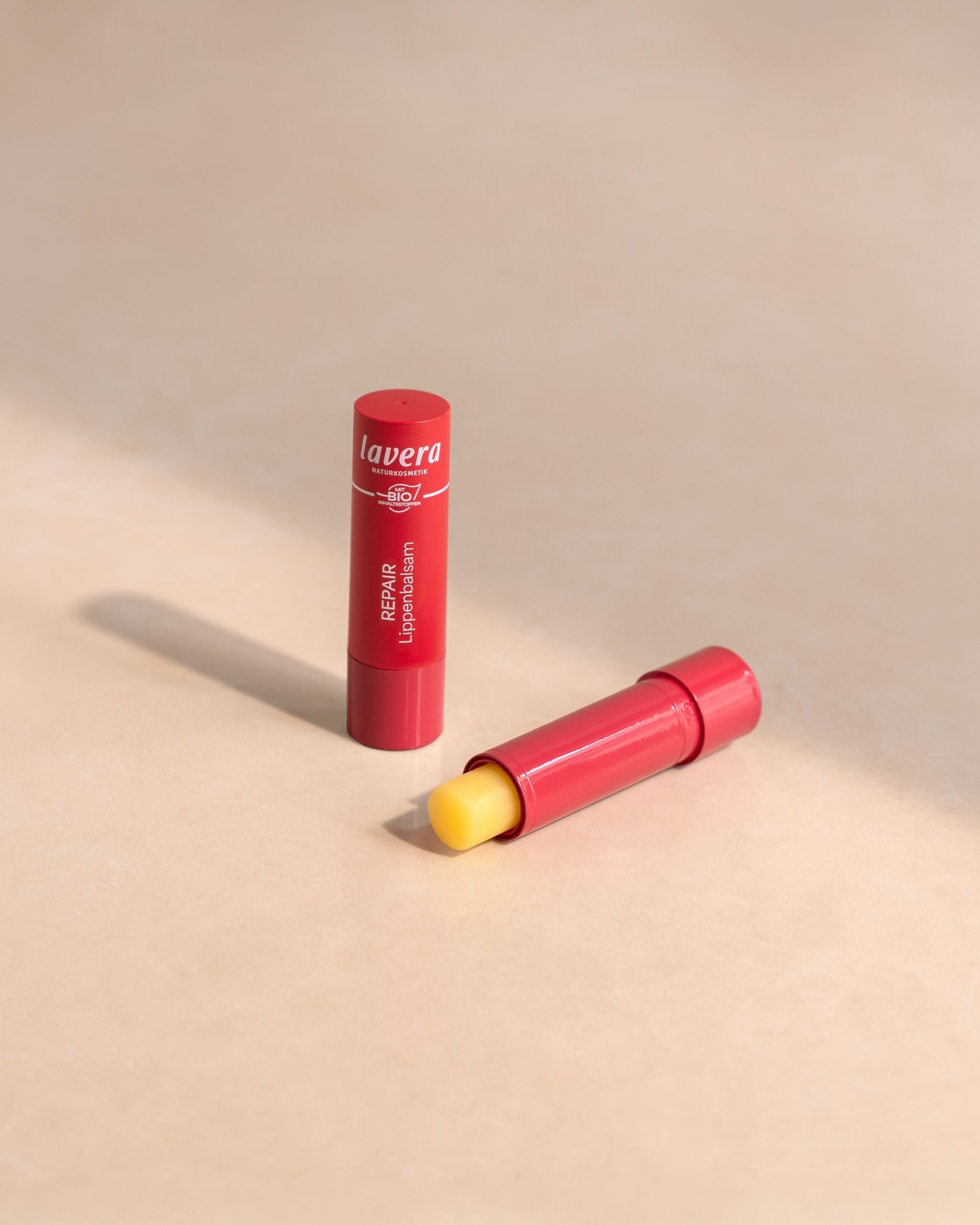 due balsami labbra lavera Repair in confezione rossa, aperto e chiuso su superficie chiara