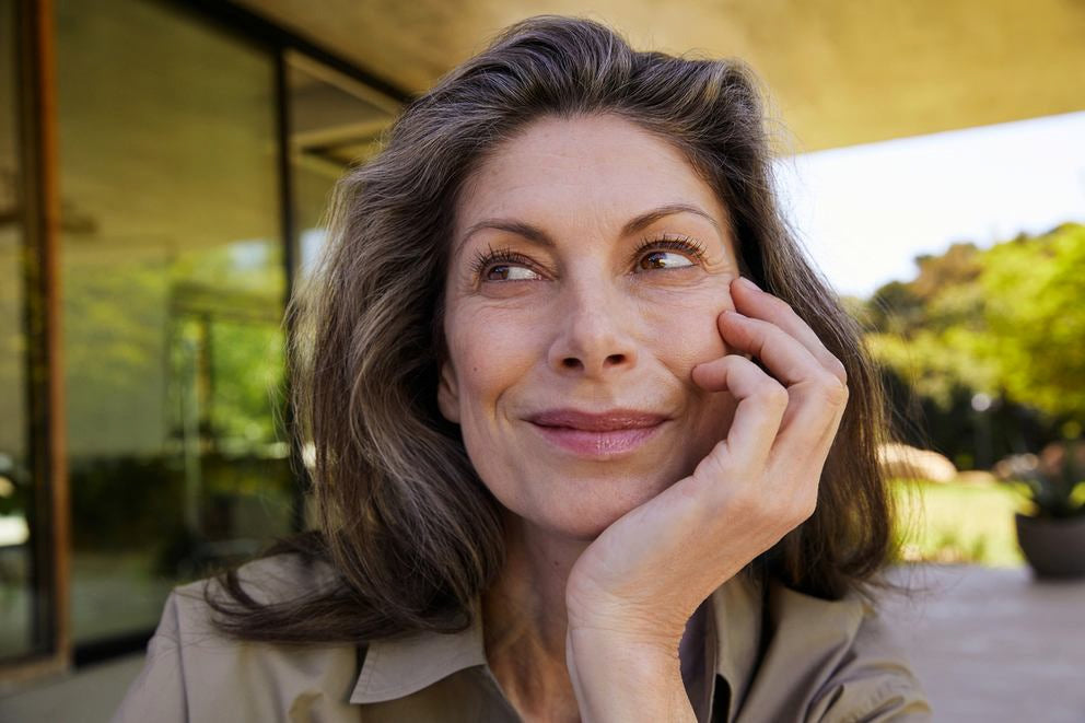 Donna matura appoggia sorridendo il mento sulla mano su una terrazza