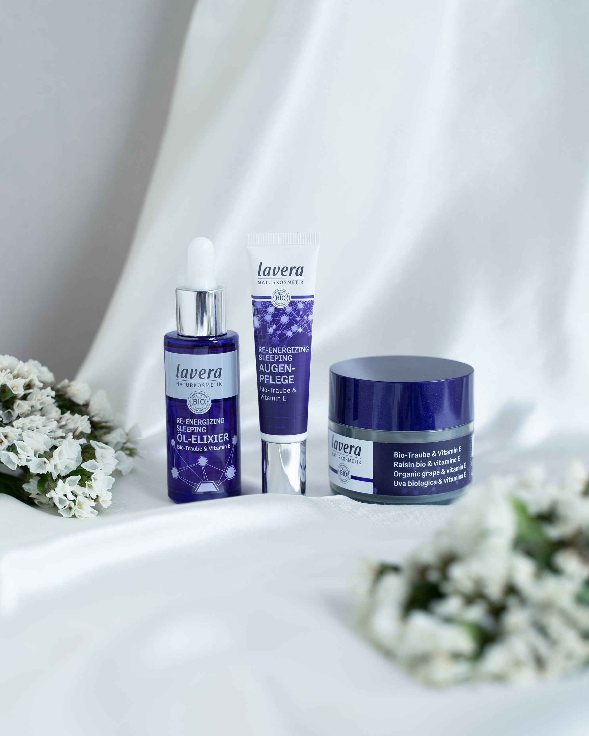 lavera Re-Energizing Sleeping prodotti di trattamento con uva bio e vitamina E, disposti decorativamente con fiori bianchi