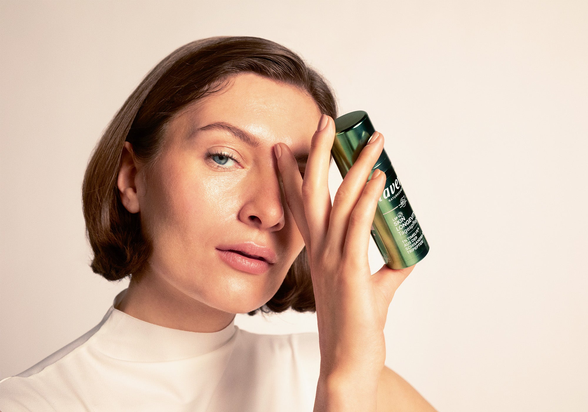 Femme aux cheveux mi-longs blond foncé tenant Skin Longevity soin de jour dans la main