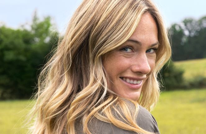 Donna bionda sorride sopra la spalla nel verde