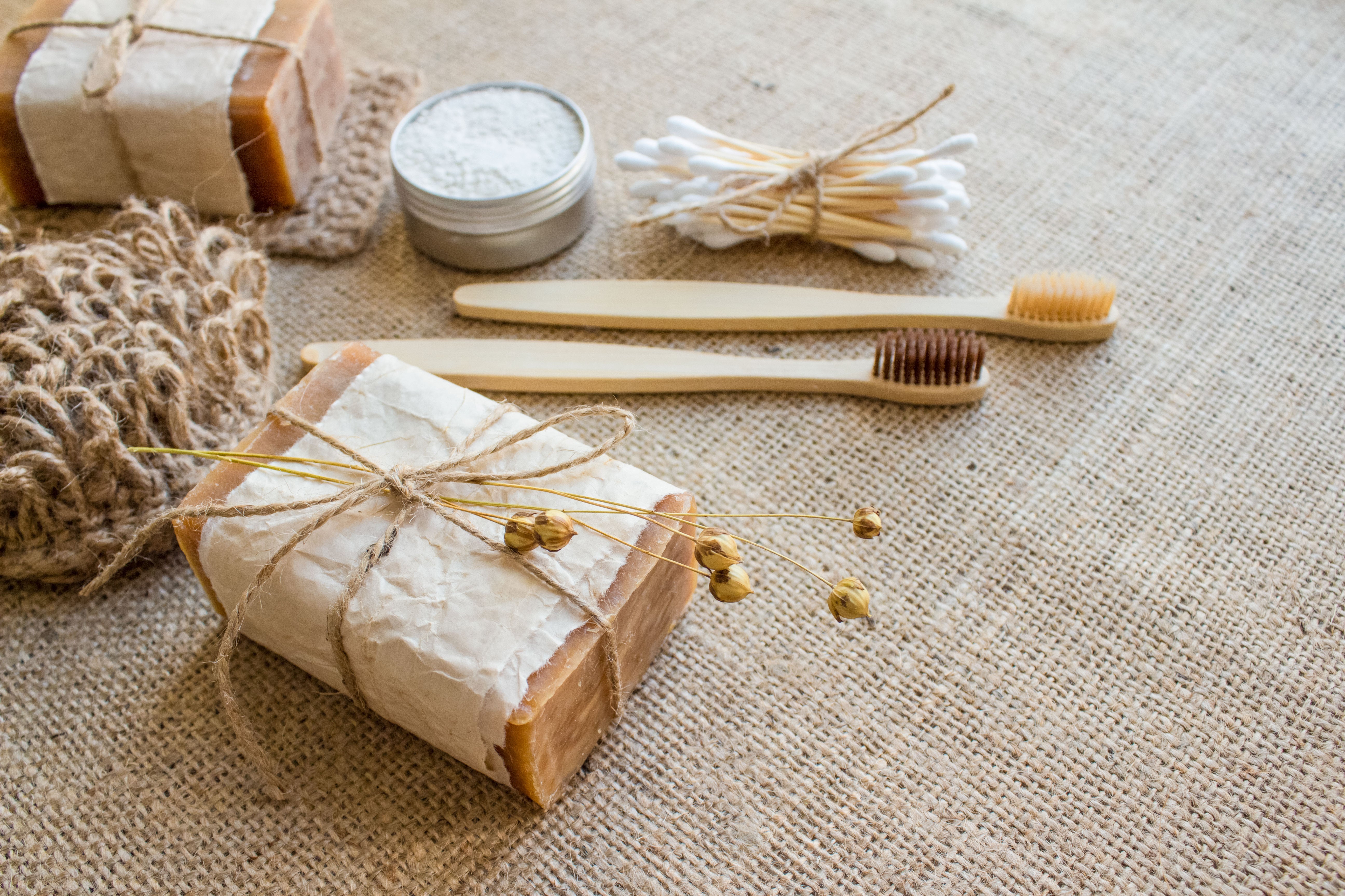 Zwei Bambuszahnbürsten, Ohrenstäbchen, Geschenk und Döschen mit Pulver liegen auf beschem Untergrund