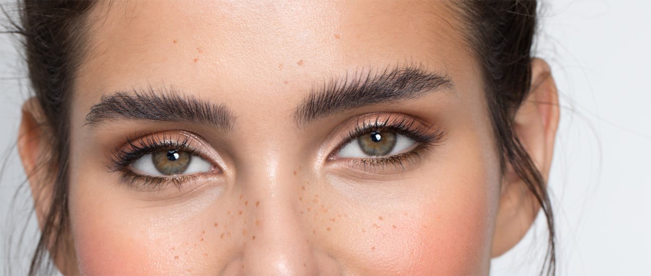 Primo piano di una giovane donna dai capelli scuri con occhi castano chiaro e sopracciglia scure definite