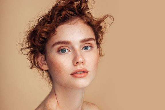 Ritratto di una donna dai capelli rossi con lentiggini su sfondo beige