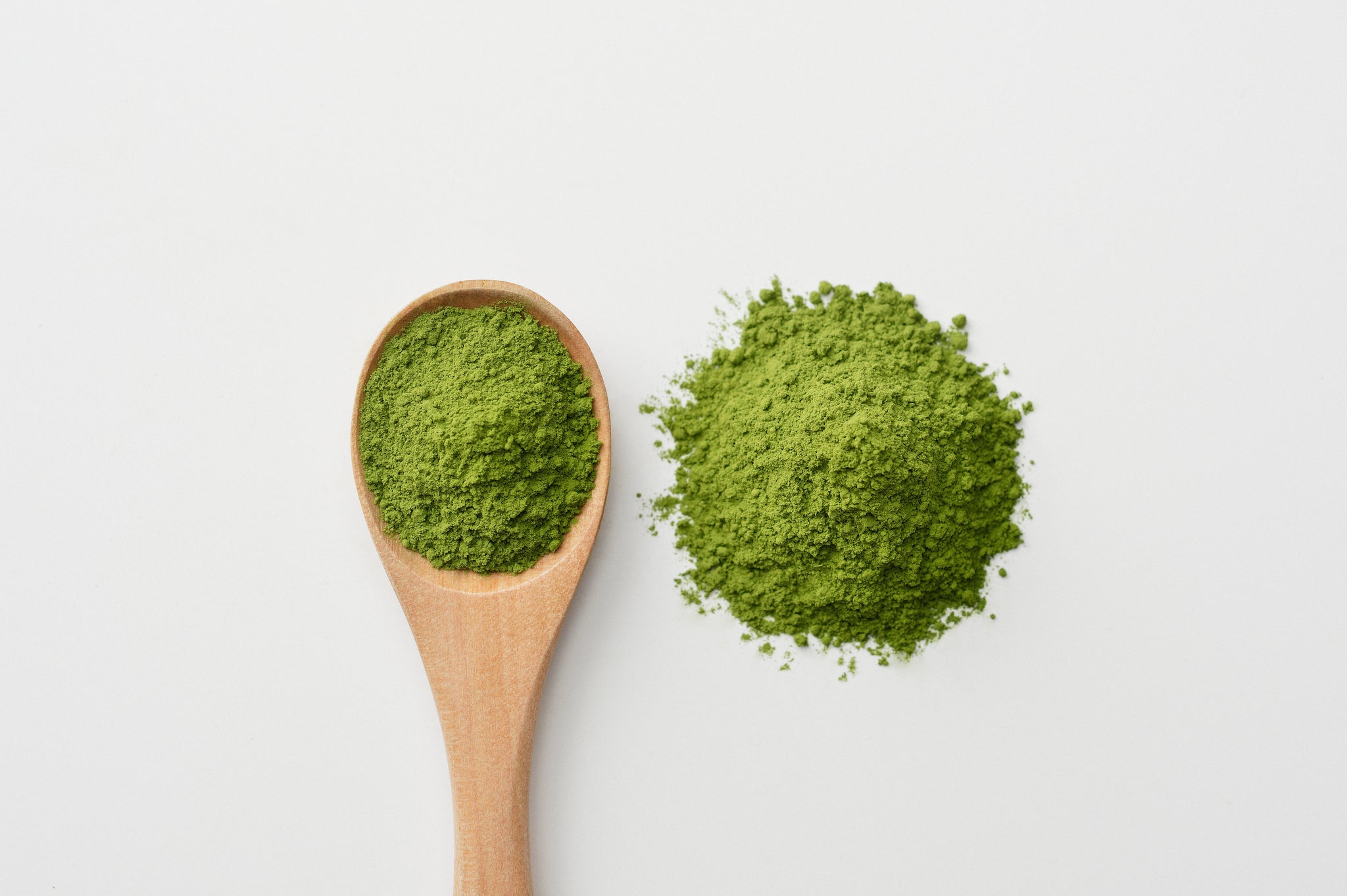 Holzlöffel mit grünem Bio-Matcha-Pulver und zusätzlichem Pulverhäufchen daneben.