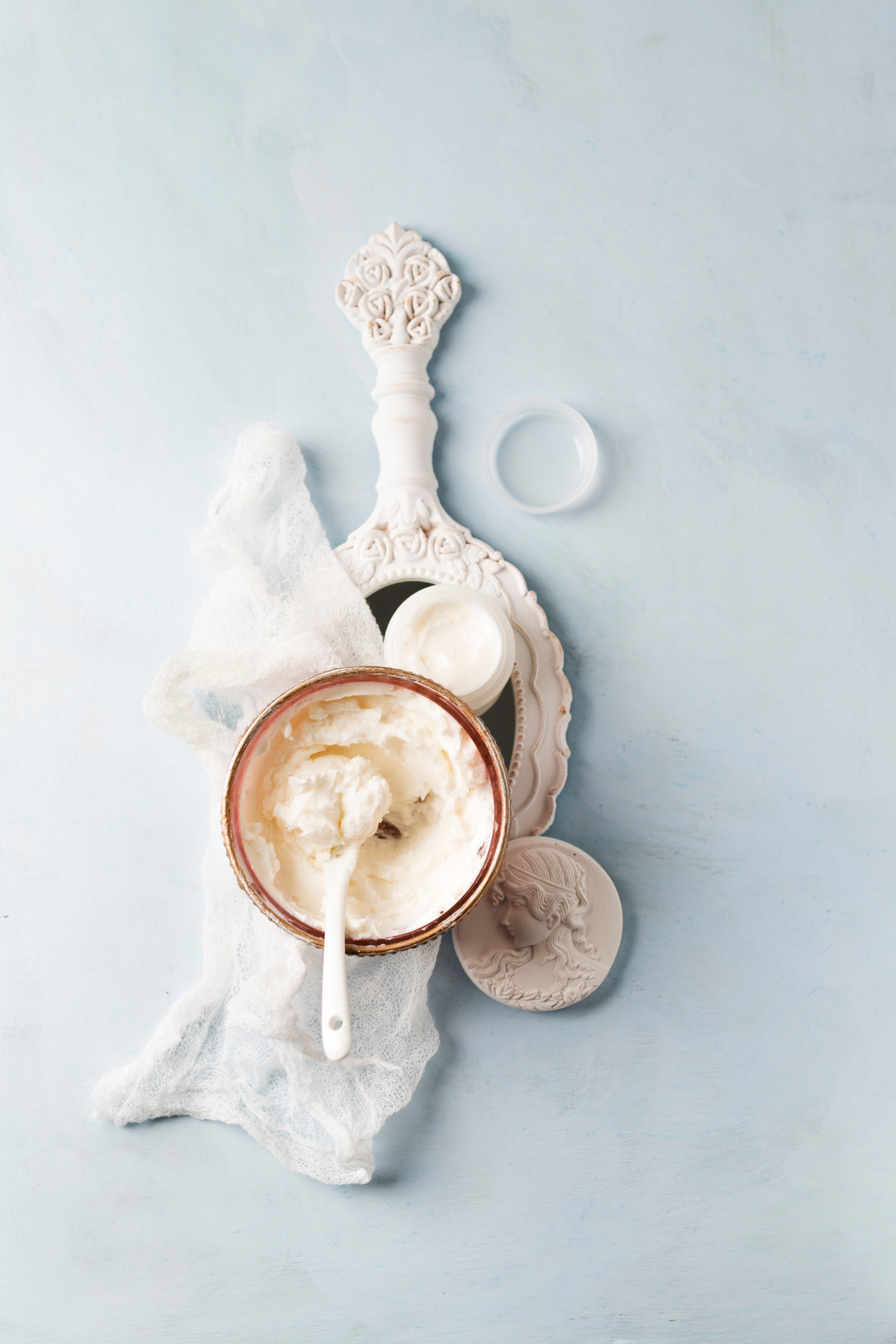 Schale mit Sheabutter und Löffel auf dekorativer Unterlage, daneben kleine Cremegefäße.