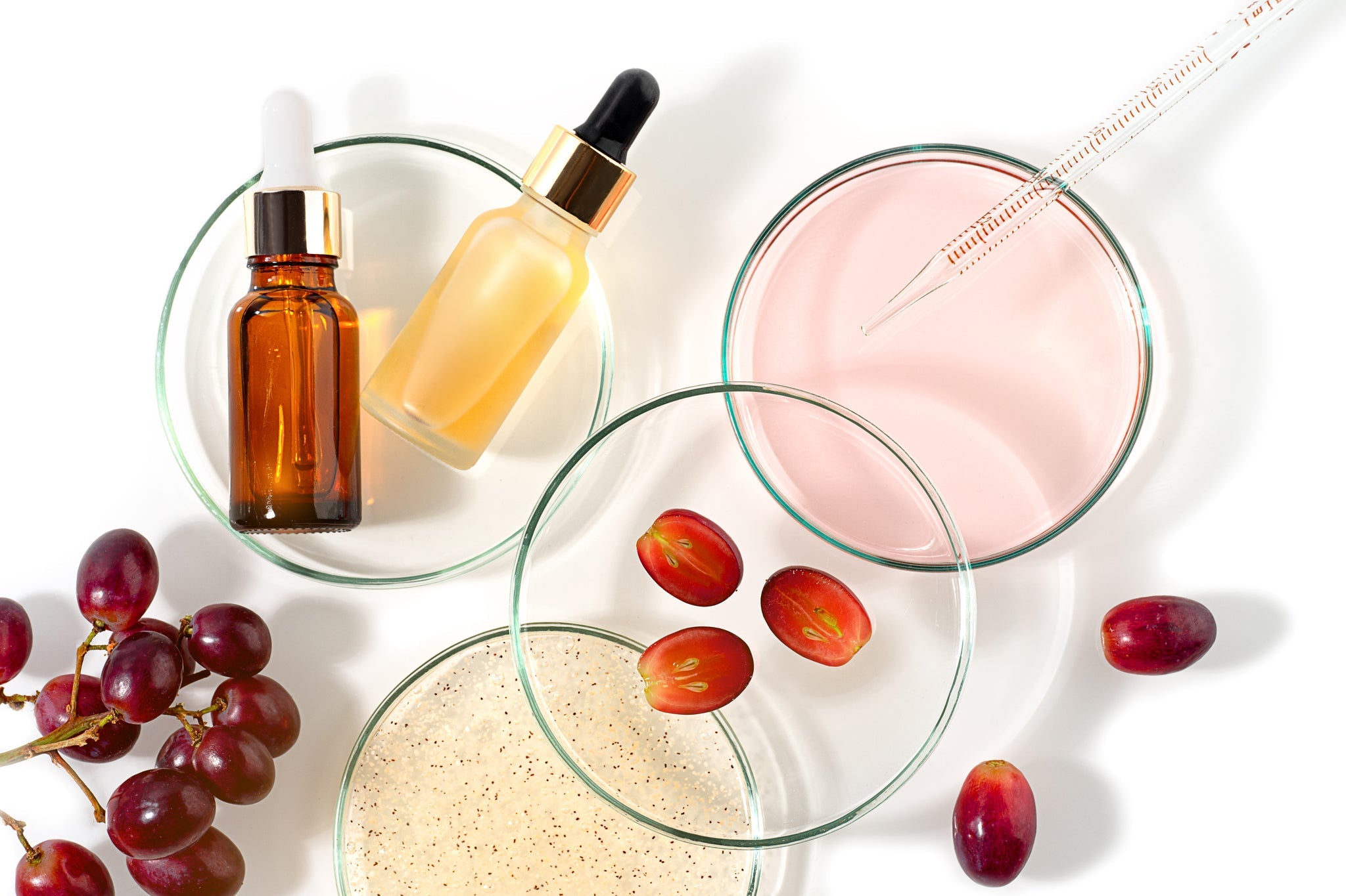 Kosmetische Darstellung mit Trauben, Laborutensilien, Pipette und Glasbehältern mit Flüssigkeiten.