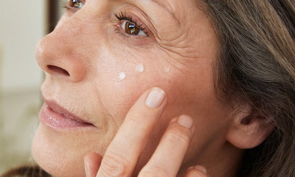 Reife Frau trägt Cremetupfer unter ihrem Auge auf