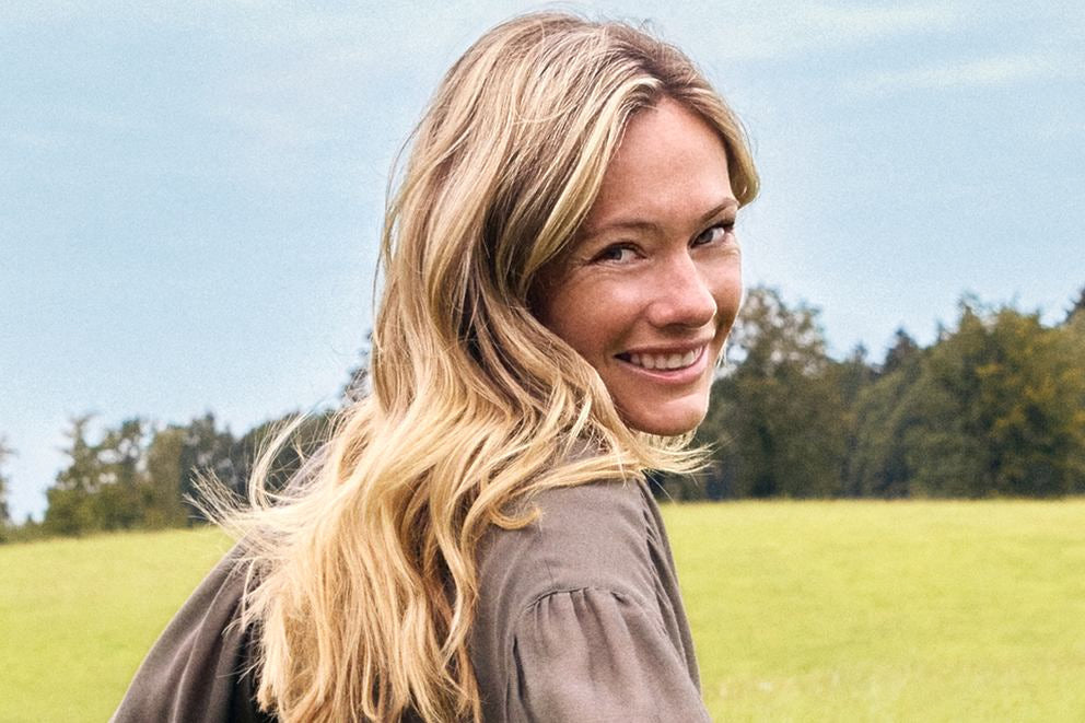 Donna bionda sorridente guarda oltre la spalla su un prato verde